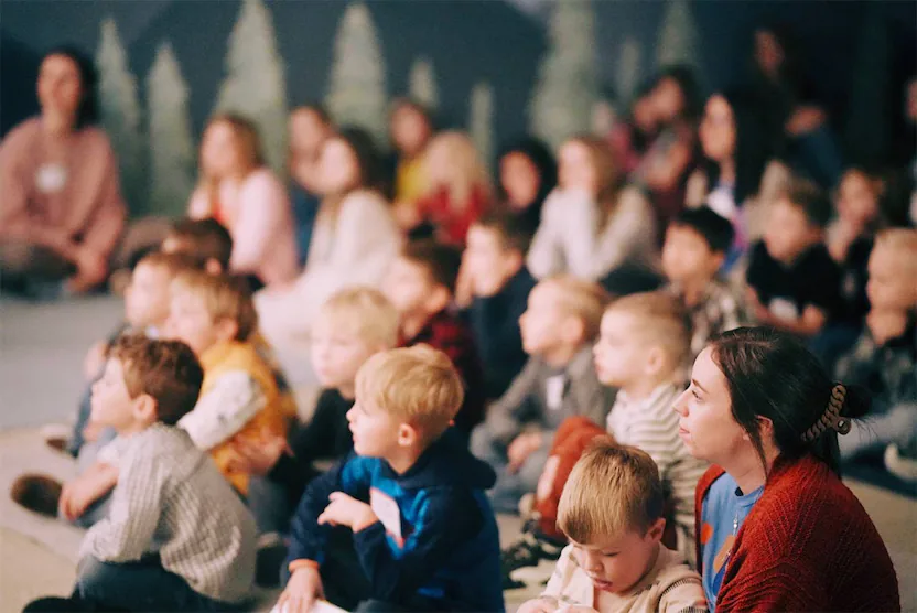 kids sitting on the ground listening to a teacher.