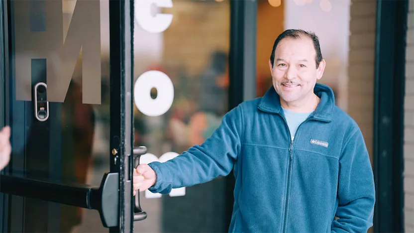 hispanic man holding open a door while smiling.