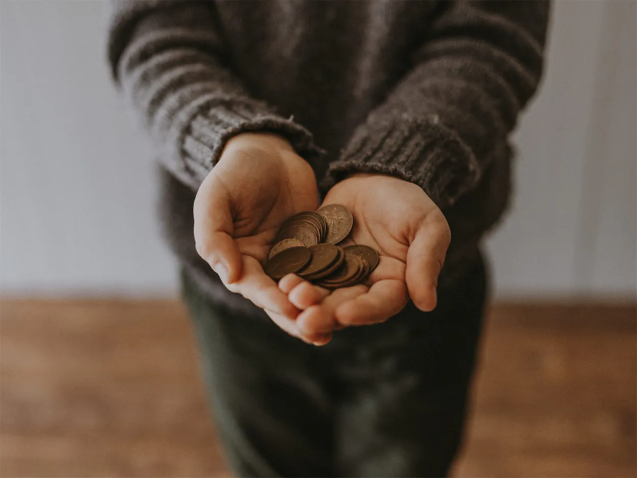 A person with hands outstretched with coins.